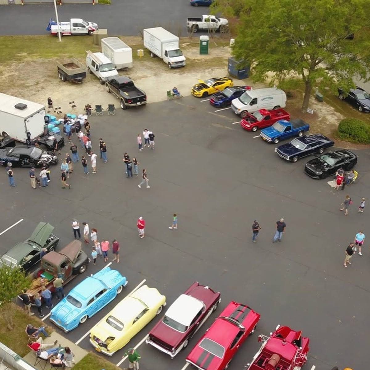 Aerial view of people attending a car show with classic and modern vehicles.