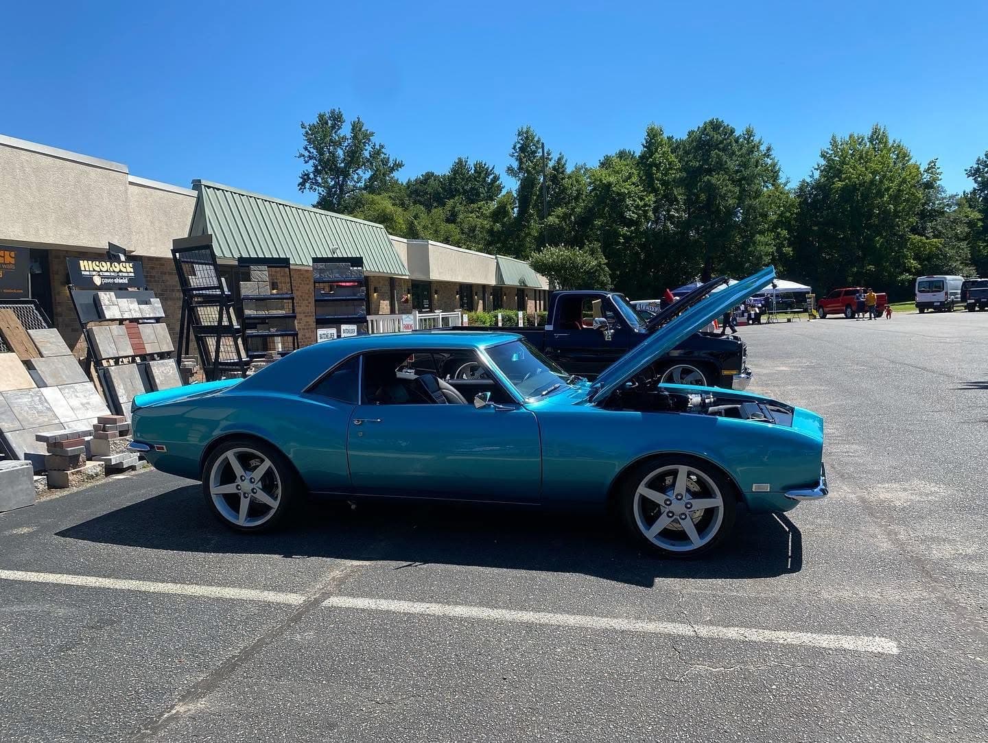 Bright teal classic muscle car with its hood open in a sunny parking lot.