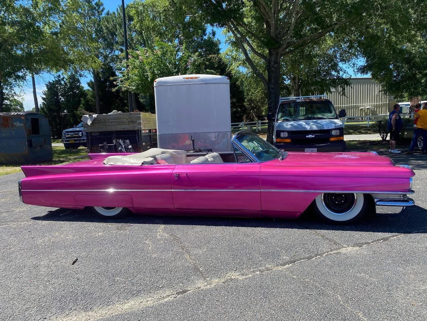 Low-slung bright pink vintage convertible with whitewall tires parked in a sunny outdoor lot.