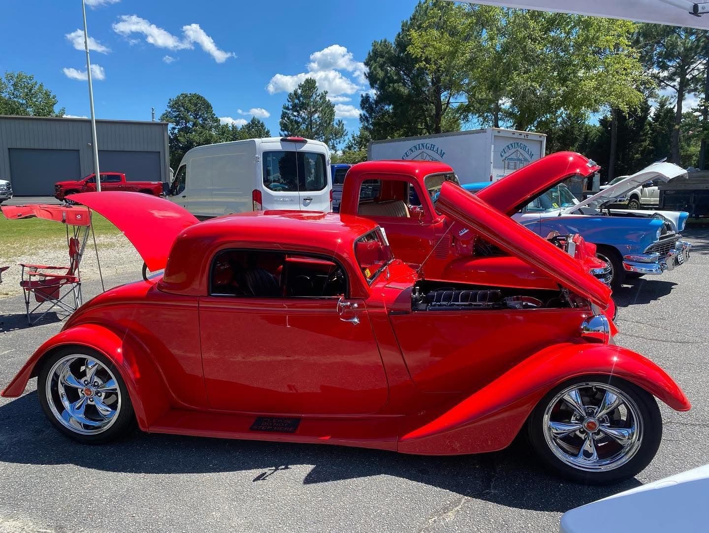 Bright red vintage hot rod with open hood and trunk at a car show.