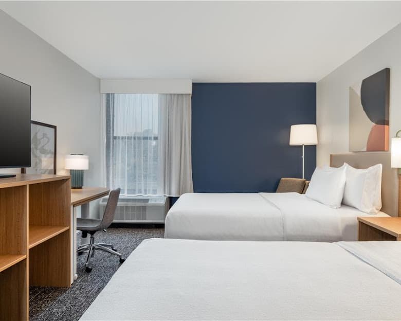 Modern hotel room with two beds, a wooden desk, and a prominent navy blue accent wall.