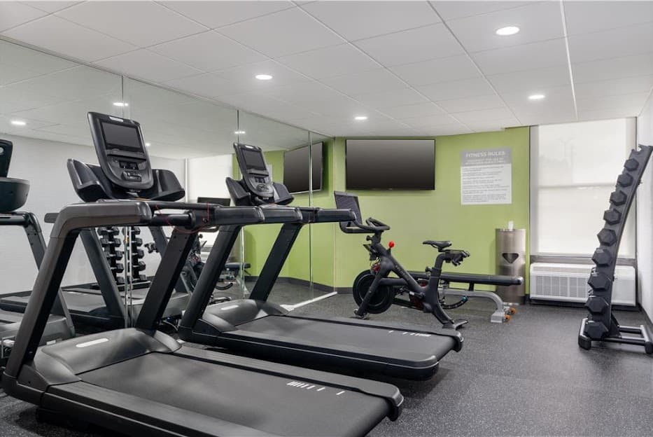 Modern hotel gym featuring treadmills, a stationary bike, weight rack, and a green wall.