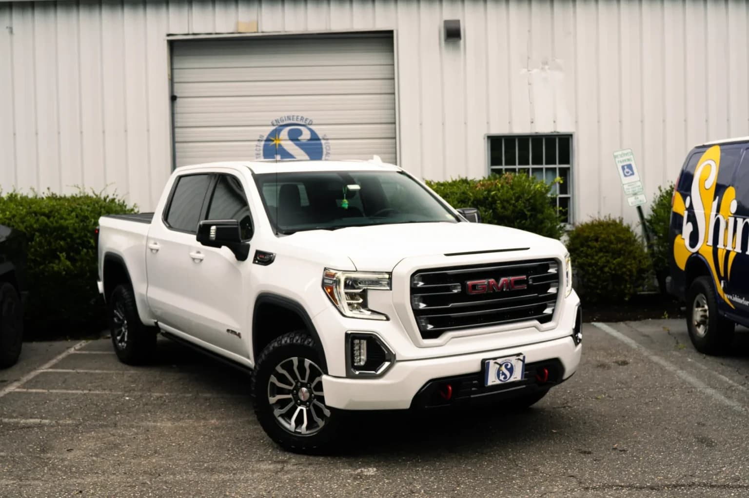 White GMC Sierra AT4 pickup truck parked in front of a white industrial building.